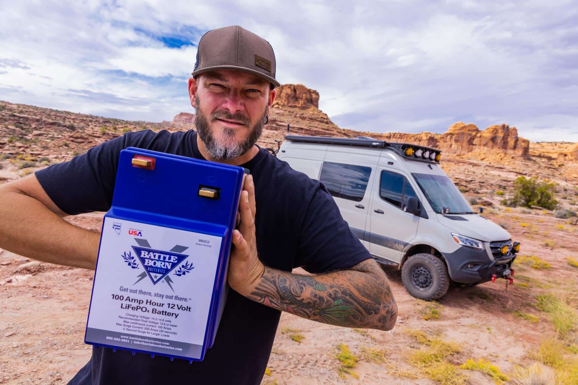 chad derosa holding lithium battery in front of overland van|truckhouse camper|DC power circuit|Be Old Later's Overland Vehicle in the Desert with Mountains in the Background|Go Play Outside Camping in the Desert