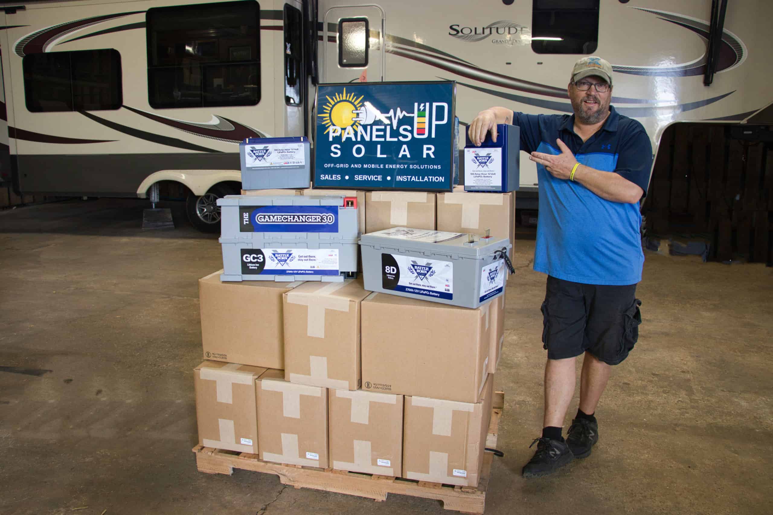 Justin Ford with a Panels Up Solar sign and Battle Born Batteries on top of boxes|Opting Out of Normal|Battle Born Batteries off grid power|Panels Up Solar Install|Justin Ford