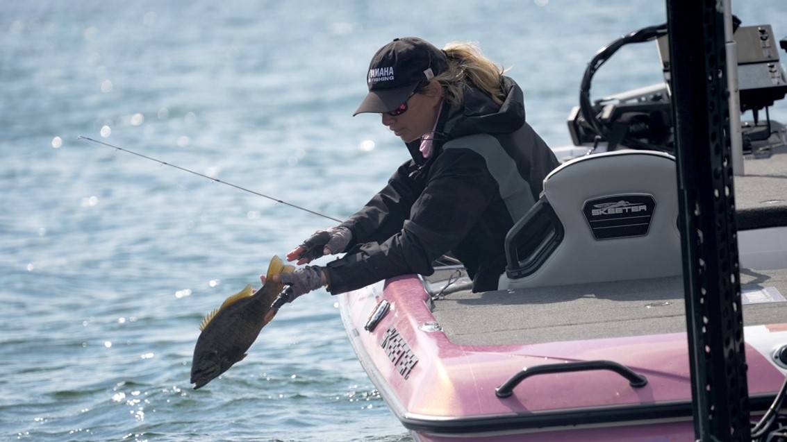 Trait Zaldain in her boat.|Trait Zaldain and two high school female anglers.|Trait Zaldain holding two bass.