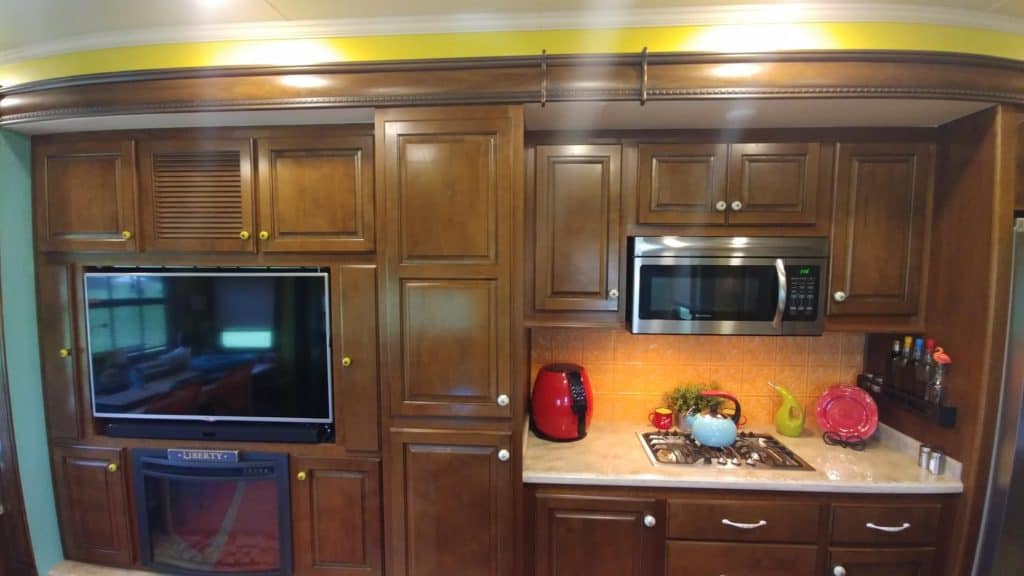 The RV kitchen is shown. There are dark wood cabinets, an oven, microwave, and stove.
