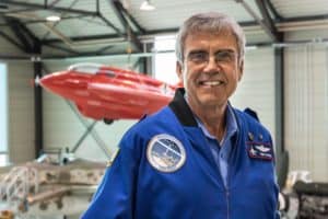 Pilot Jim Payne is standing in an airplane hangar and smiling.