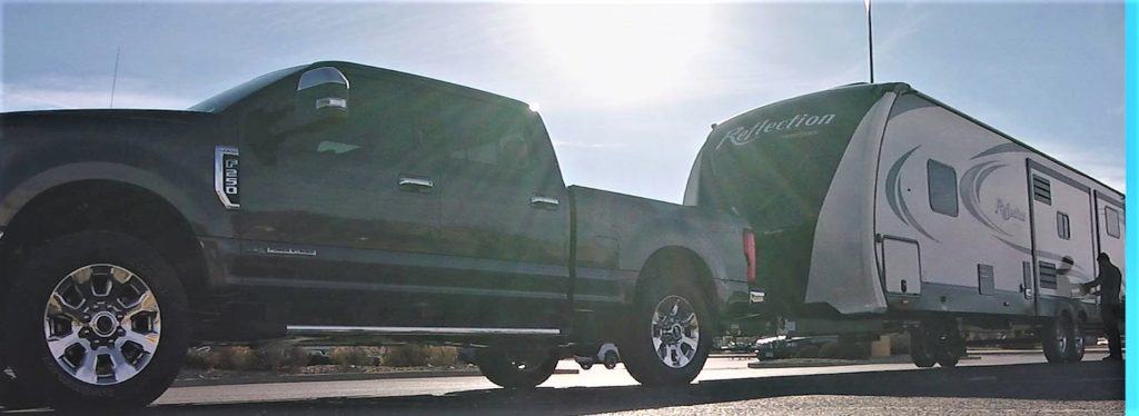 A dark colored Ford F150 is towing a large RV.