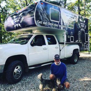 Rick Clunn Truck Camper Wrapped in Battle Born Battery branding. He is petting his dog in front of the camper