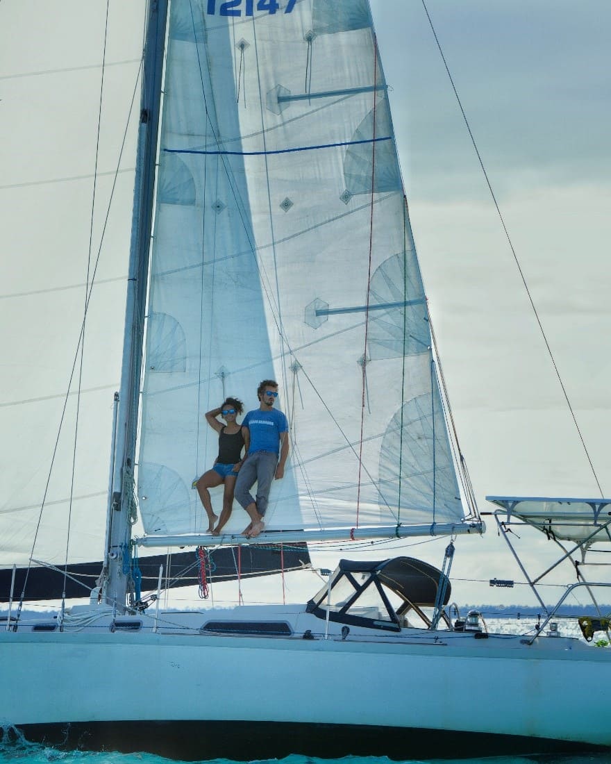 Two people sitting on a sailboat sail.
