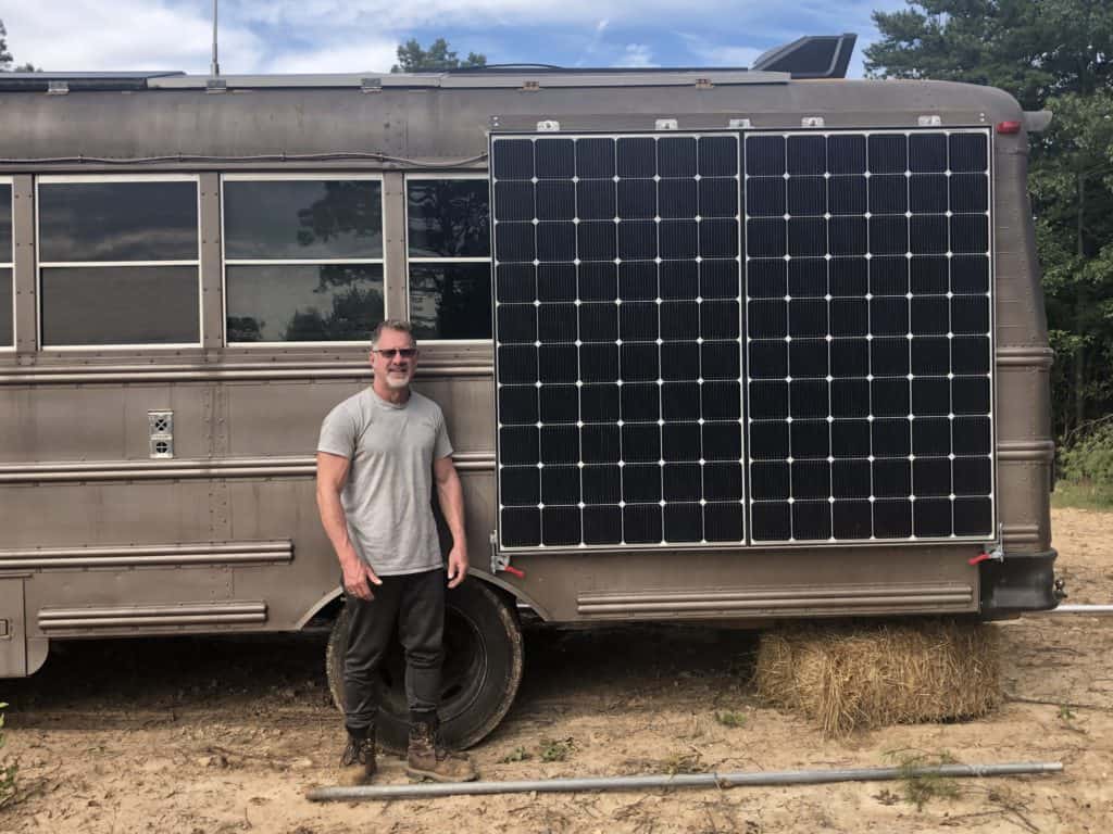 A man standing in front of a school bus with a solar panel on it. 