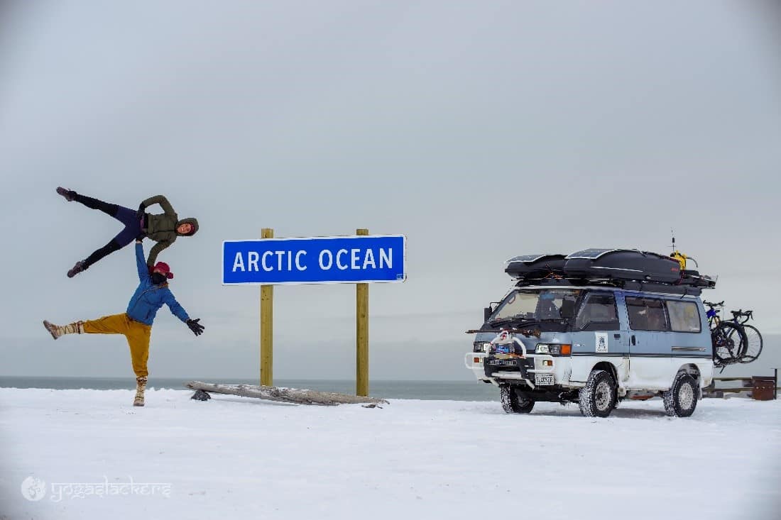 YogaSlackers doing a yoga pose in front of an "Arctic Ocean" sign with their van next to them