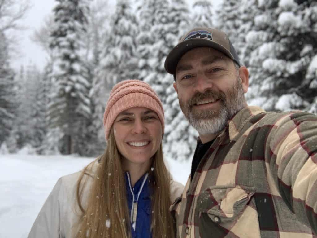 Two people standing in a snowy forest. 