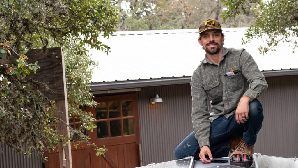 A photo of Andy Rawls on the roof of the trailer working on solar panels