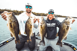 Brian Robison and Sam Feider kneeling on a bass boat holding 4 bass fish that they caught