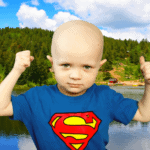 Child wearing a Superman shirt flexing his muscles in front of a lake