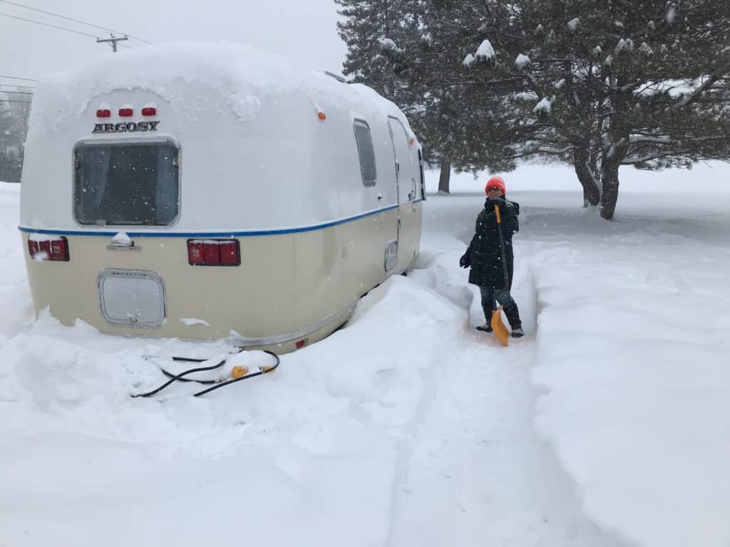 Crystal shoveling snow around her Airstream Argosy trailer, Zola. Vintage campers are cozy in the snow.