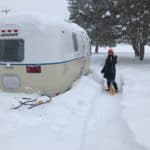 Crystal shoveling snow around her Airstream Argosy trailer, Zola. Vintage campers are cozy in the snow.