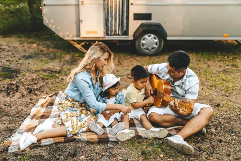 family sitting on a blanket while the father plays the guitar