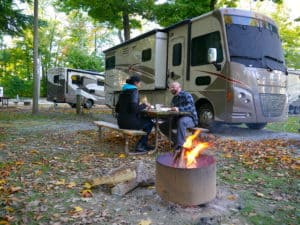 Sabrina and Kenny camping with a fire in the foreground and their Winnebago Vista LX 27N in the background.