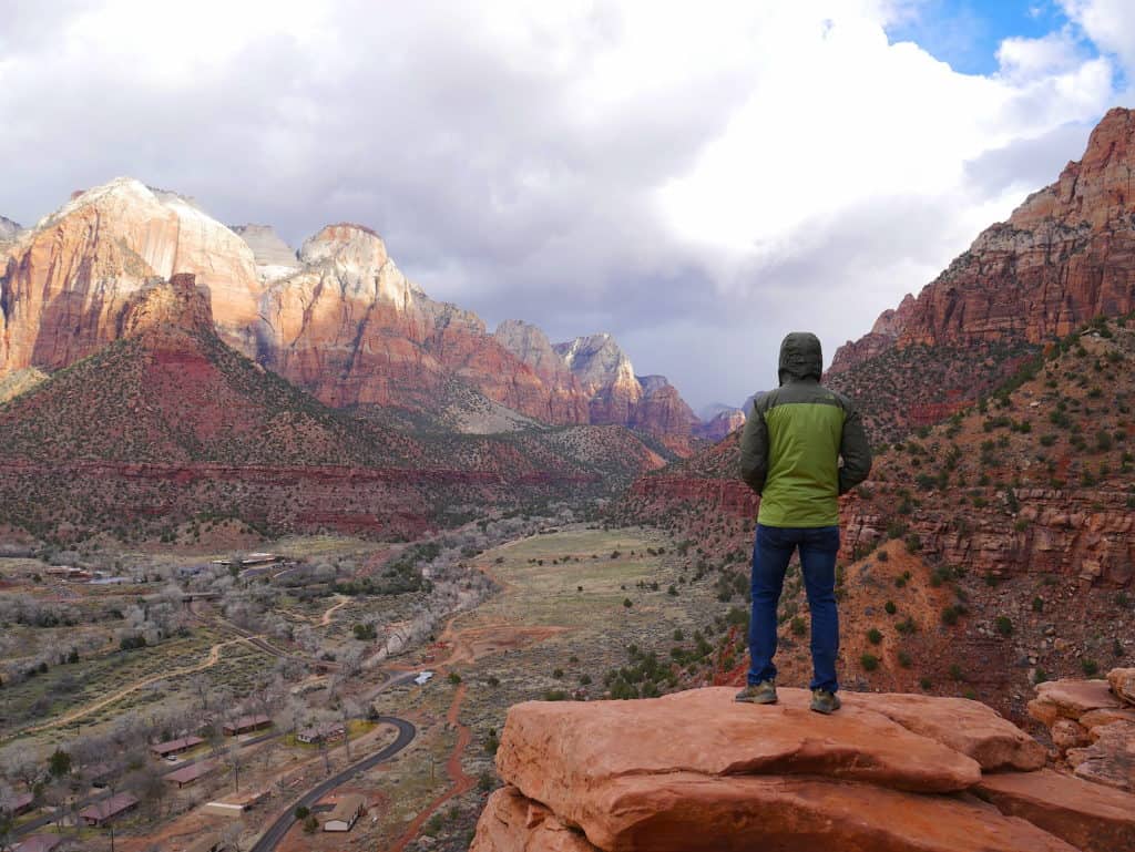 Sabrina in a hooded jacket enjoying the view of a mountain range in Zion National Park. 