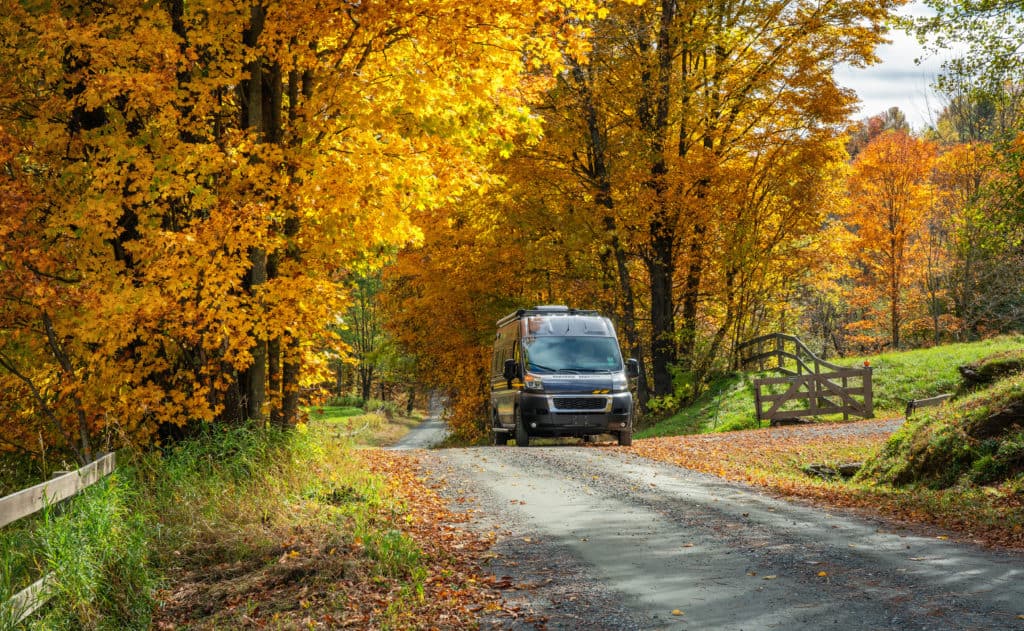 Class B RV driving down the road with fall foliage in the background