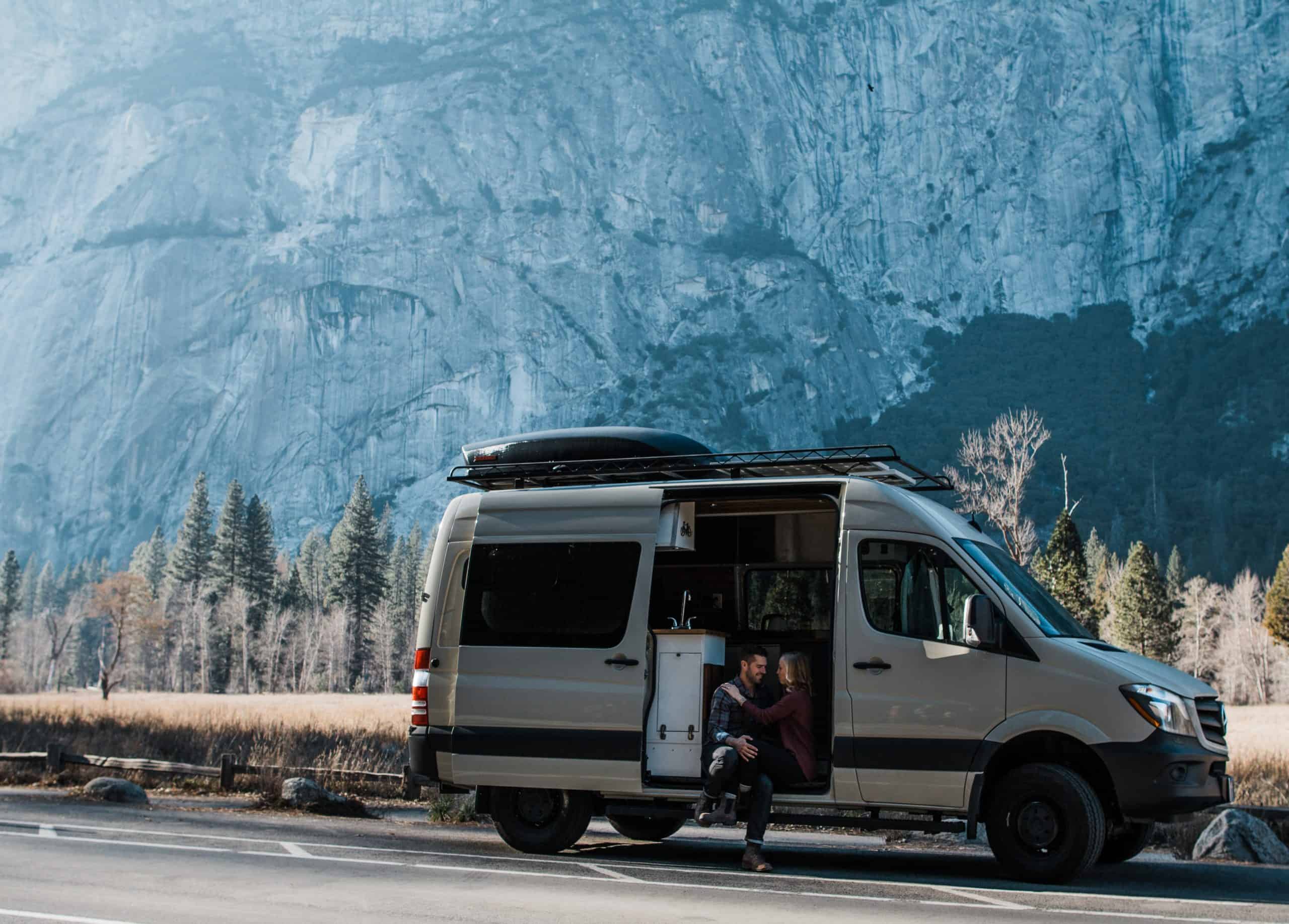 Couple embracing in the door of their overlanding van in front of mountains