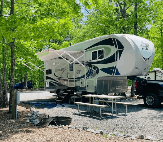 fifth wheel rv at campsite with green trees