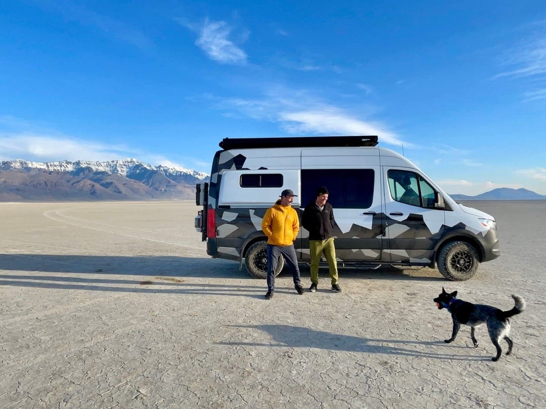 Couple standing outside of their sprinter van while looking at their dog