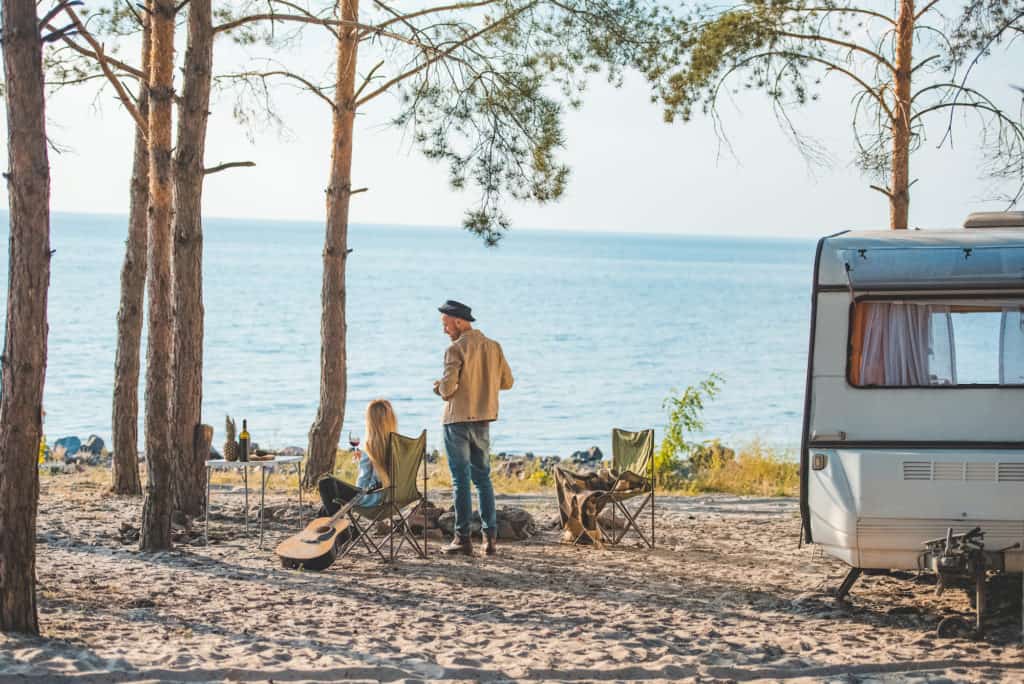 Two people camping on a beach with a travel trailer