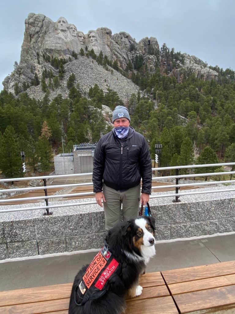 John holding his dog on a leash in front of Mount Rushmore