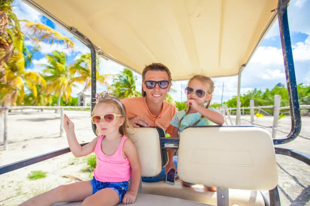 family riding electric golf cart in tropical location