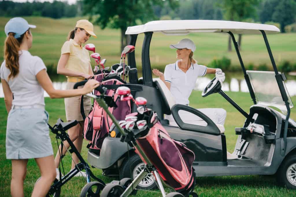 Women with pink golf clubs standing around a golfcart that one woman id driving
