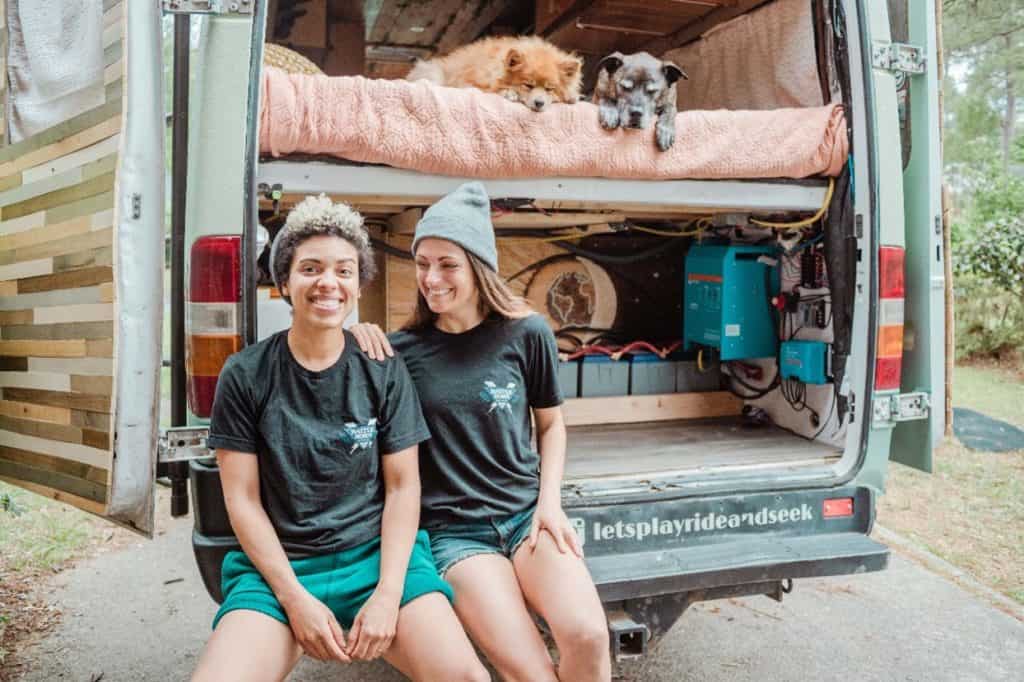 Natalie and Abigail sitting in the back of their Sprinter van with their dogs