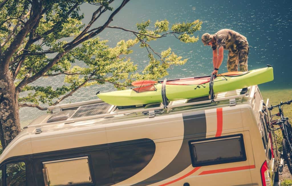 A man loading his kayaks onto his van with a lake in the background