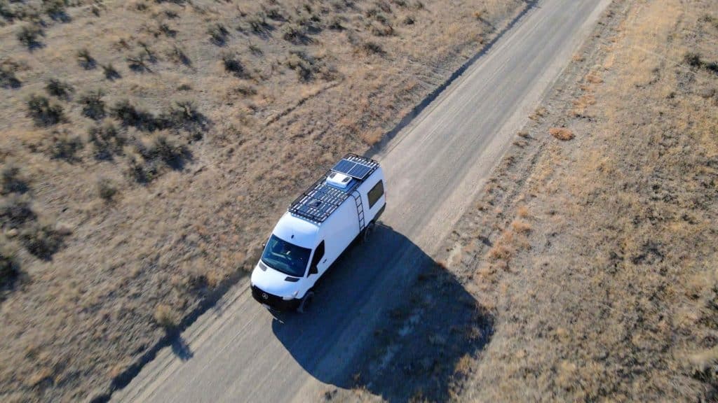 Drone shot of a Sprinter van with a solar panel on top driving on a back road