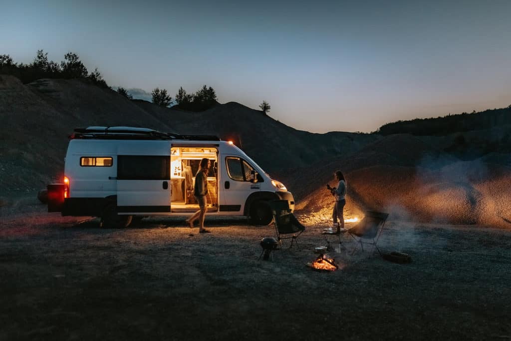 Couple around a camp fire and their converted van
