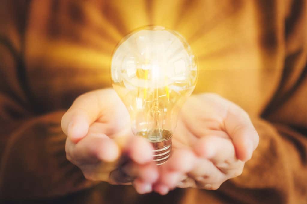 closeup of two hands holding a light bulb that has been edited to light up 