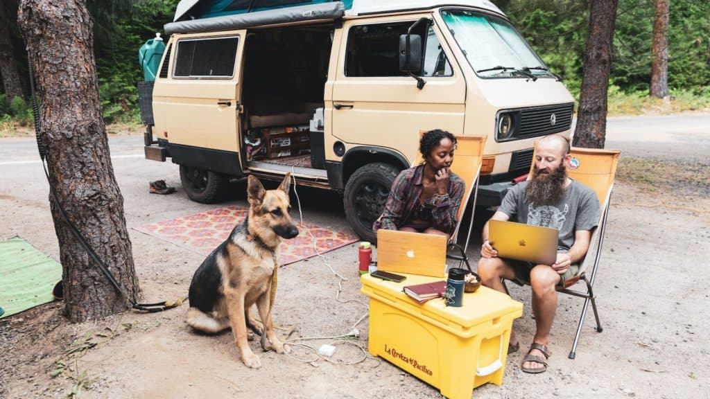 Noami and Dustin working on laptops with their German Shepard outside of their rig