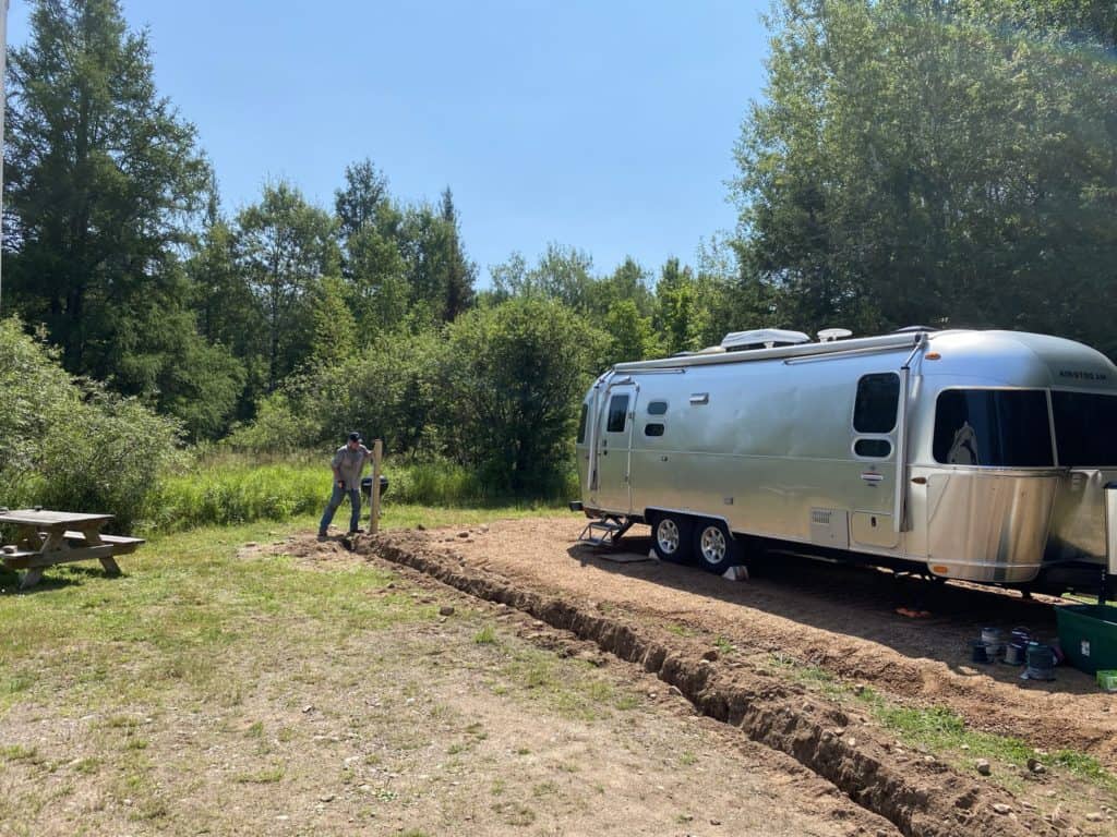 Man putting a post in the ground next to an Airstream trailer at Camp Hackett