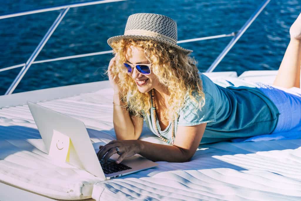 woman remote working on laptop and cell phone on a boat