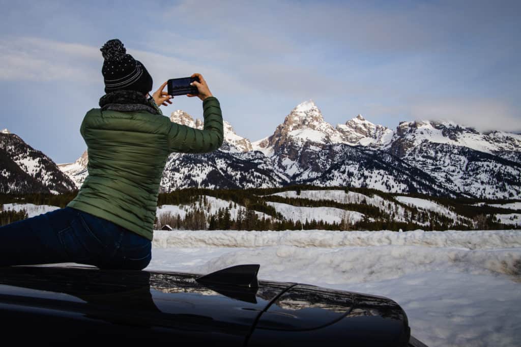 Woman wearing winter clothes taking a photo of the Grand Tetons