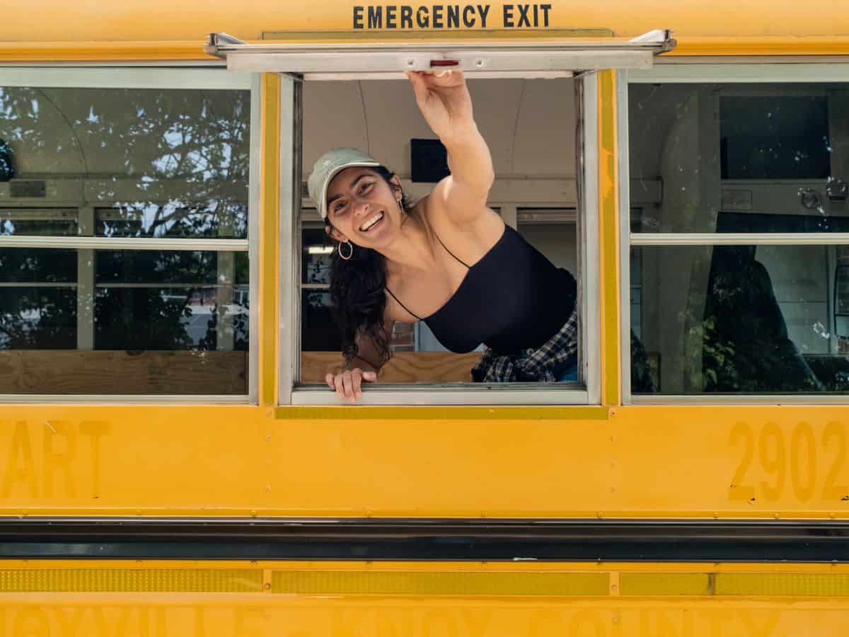 Leah Judson opening a window and smiling on her skoolie