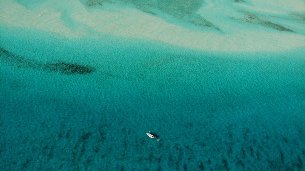 high aerial shot of a sailboat on teal water