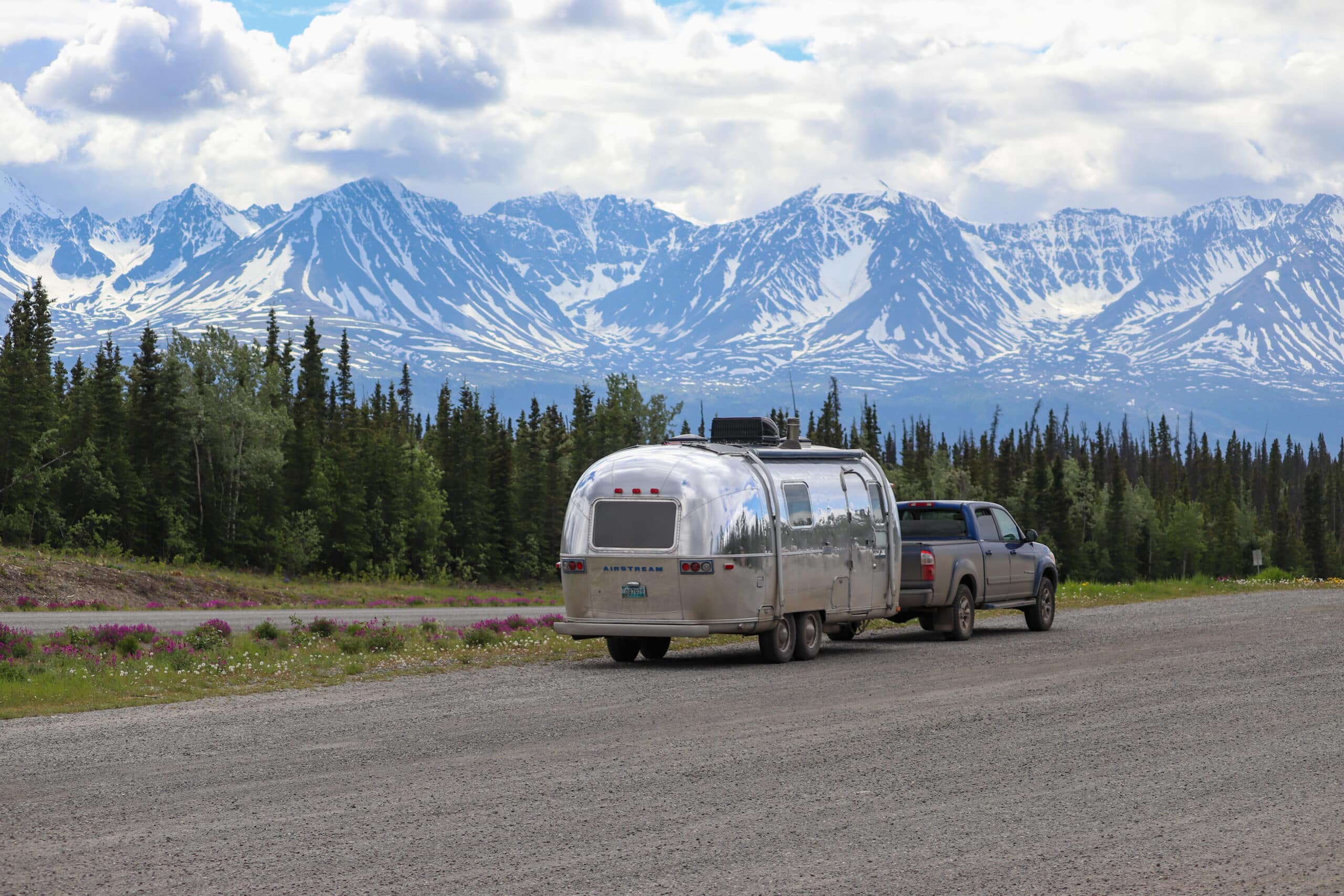 Slow Car Fast Home's Airstream on a Road in Alaska Surrounded by Snow-Covered Mountains