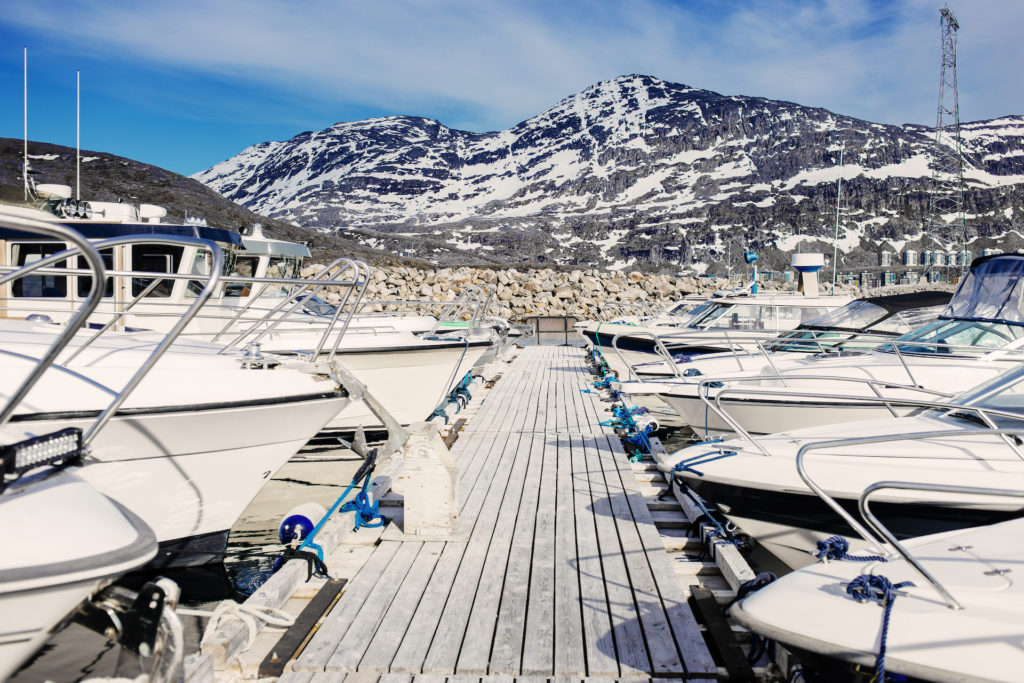 Boats moored by pier at harbor against mountains