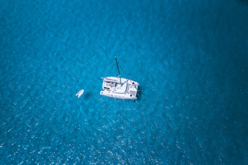 Aerial drone photo of catamaran sailboat at blue clear ocean water