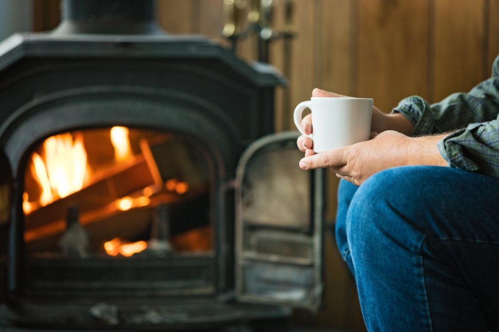 man holding mug with wood stove heating in background