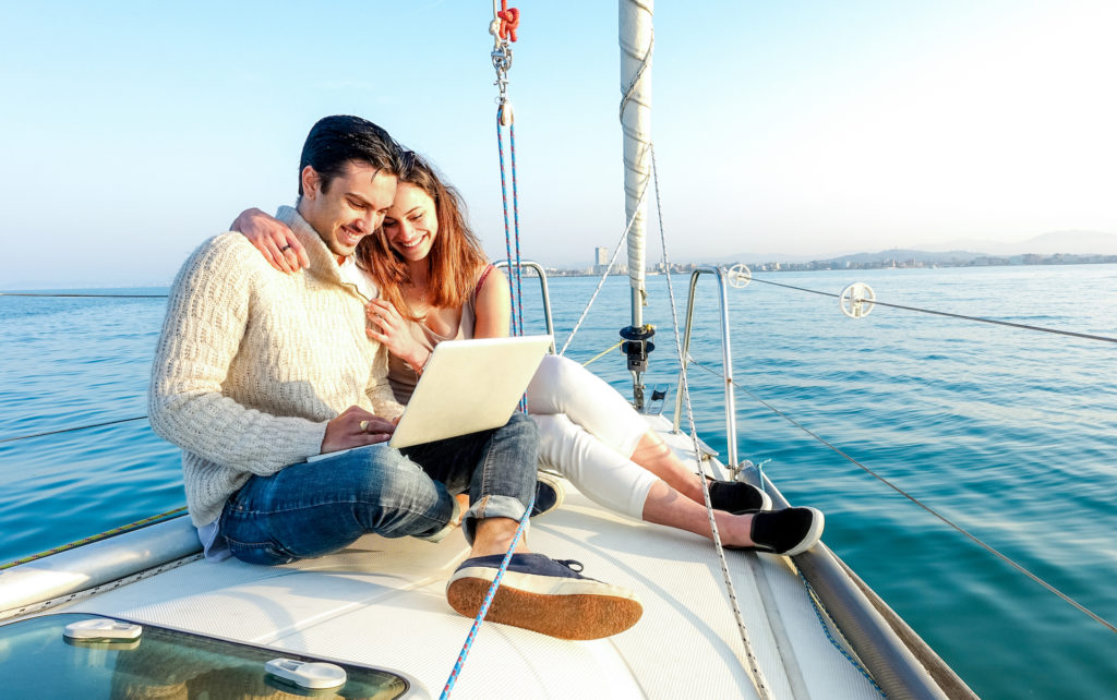 Young couple in love on sail boat having fun remote working at laptop