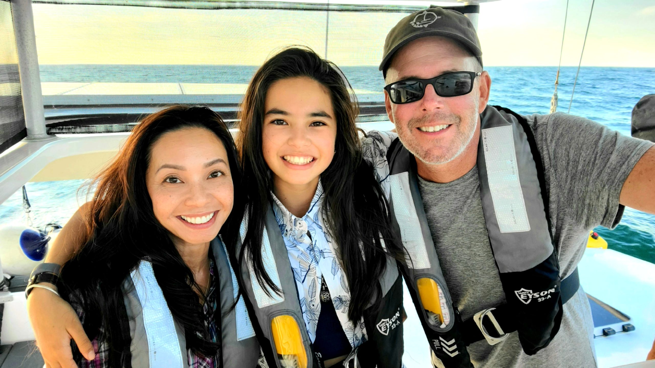 Teal, Linh, and Emma smiling for a photo on their sailboat