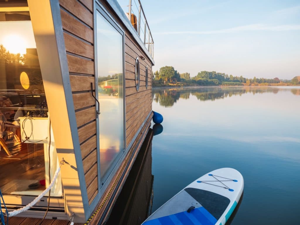 houseboat moored on a pier with paddleboard on a river in a early sunny morning