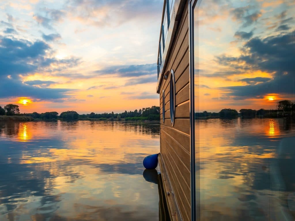 Sunset behind houseboat on a river. Sunset is reflecting in a window of a floating house in a warm summer evening