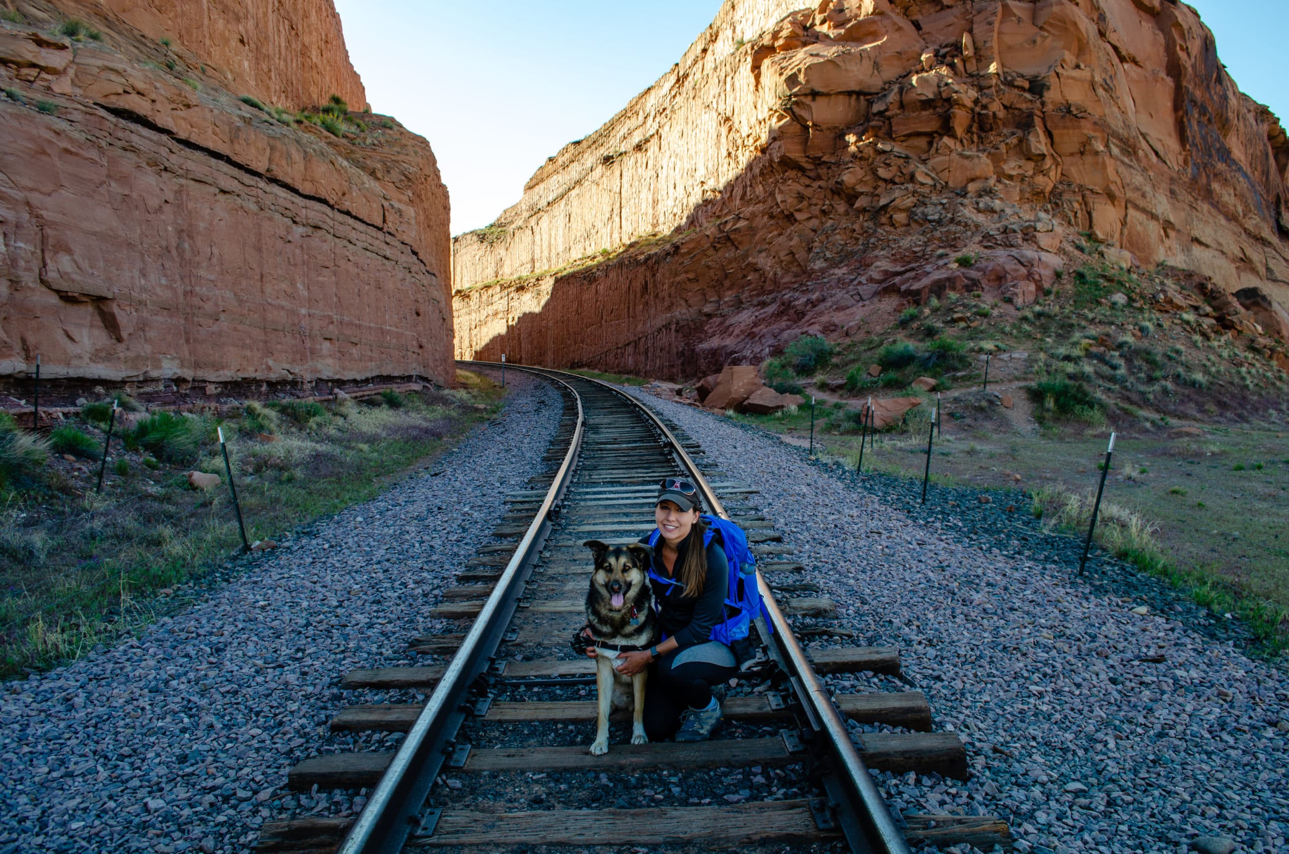 Cass and Jasper from Tails of Wanderlust in Front of a Mountain on Old Train Tracks