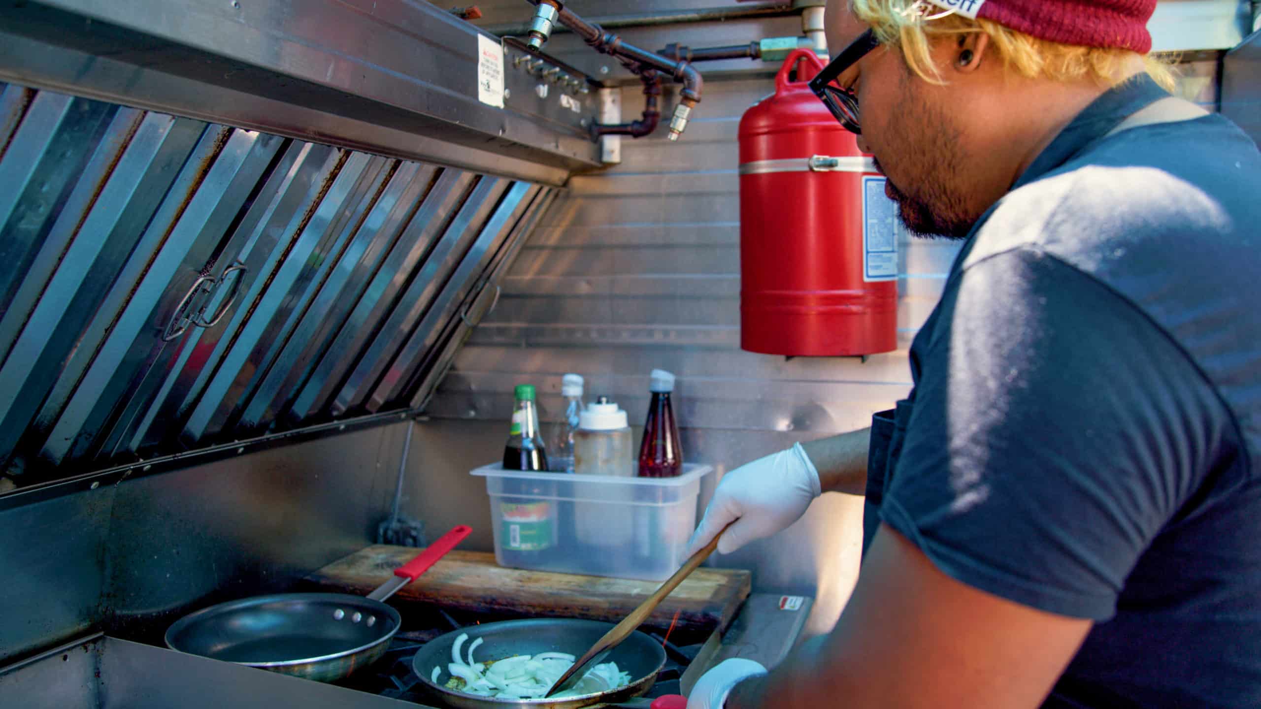 Pari cooking onions in a pan inside of his food truck