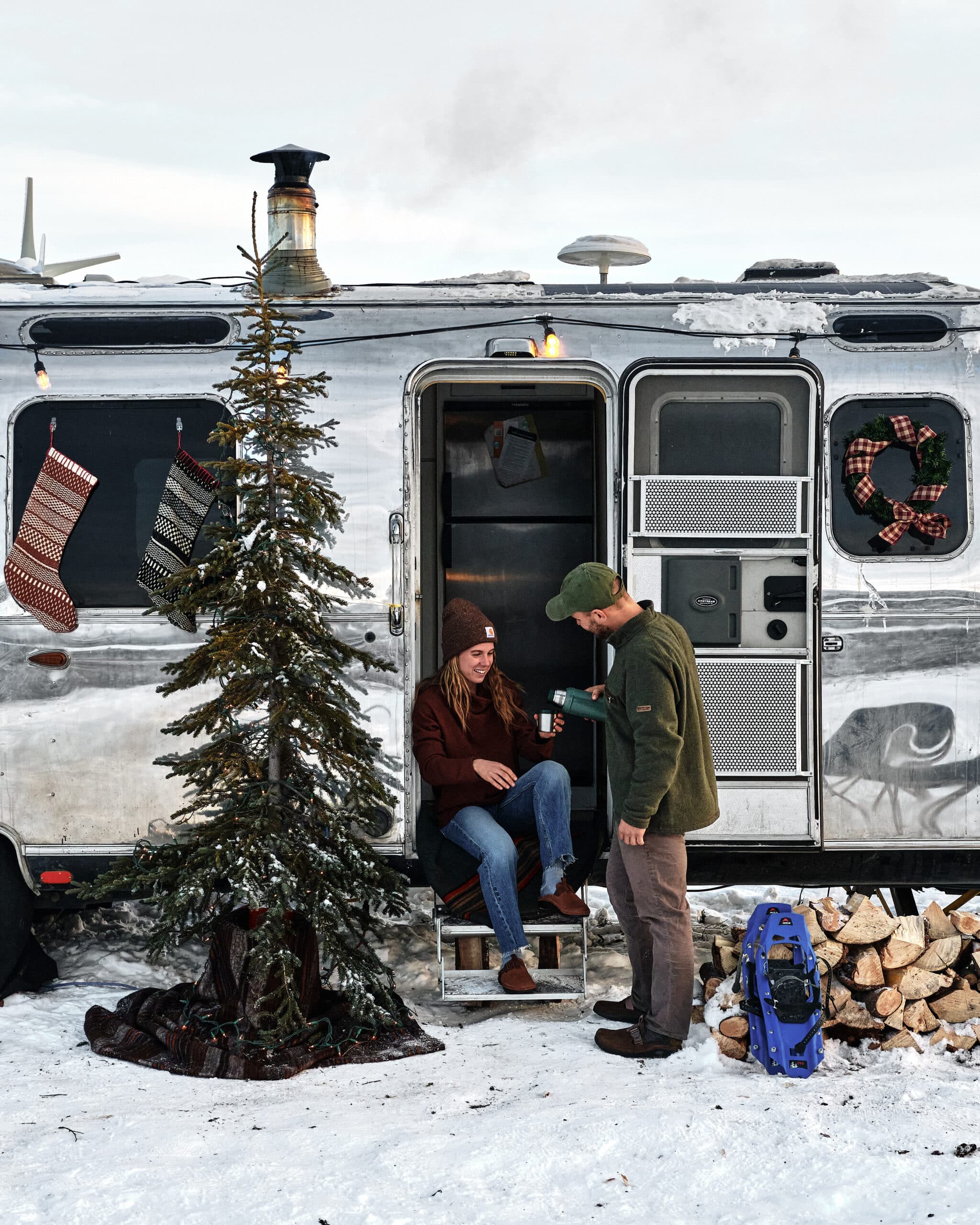Two People Enjoying a Hot Drink in Front of Airstream with a Christmas Tree in Front