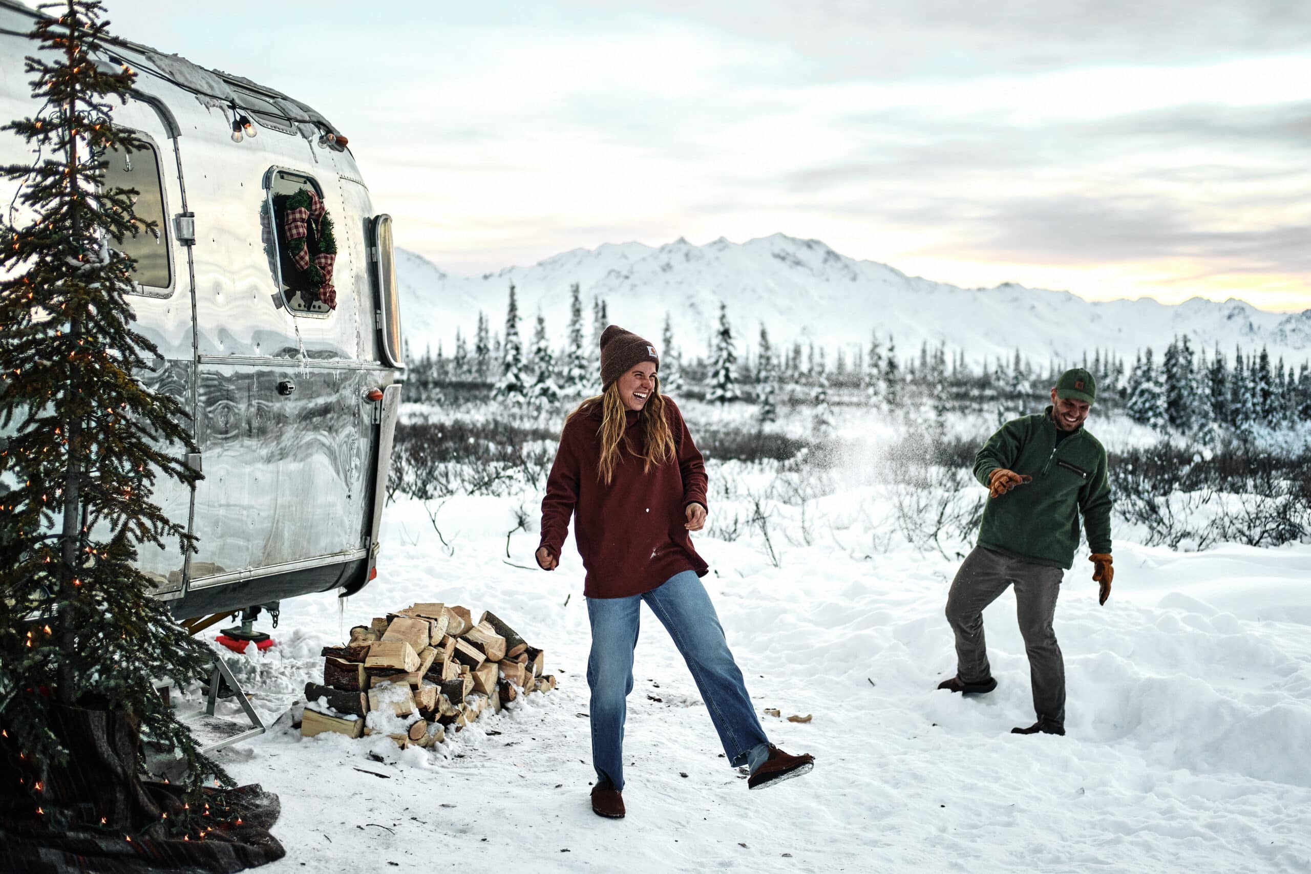 Two People Having a Snowball Fight Next to an Airstream with a Christmas Tree in Front